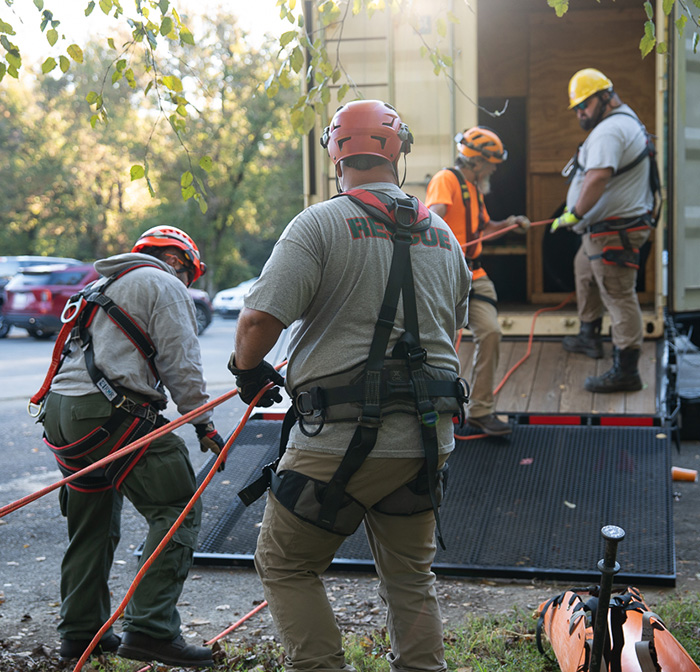 A group of first responders hold ropes outside of a confined space simulator trailer.