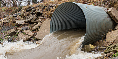 A large stormwater drain spills water into a ditch.