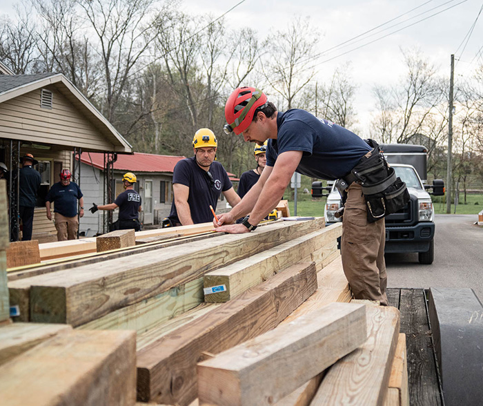 First responders measure long pieces of lumber for a structural shoring activity.